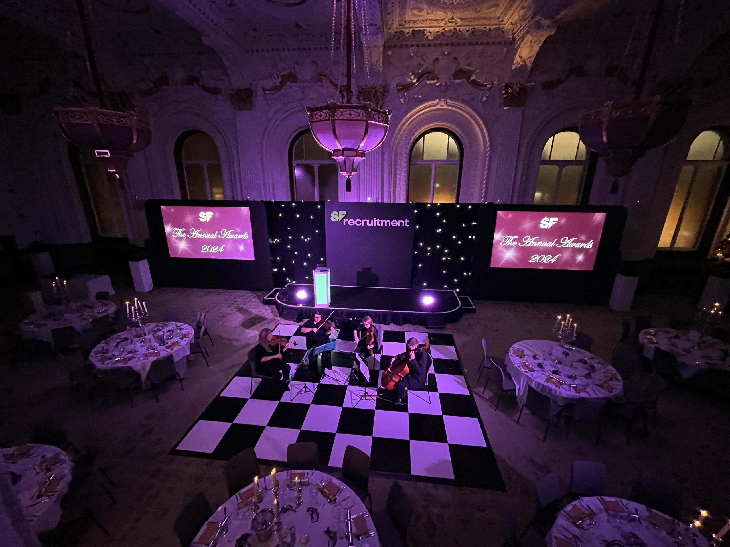 SF Recruitment at the Grand Hotel Birmingham, with a a string quartet seated on a black and white checkerboard floor area and large screens in the background.