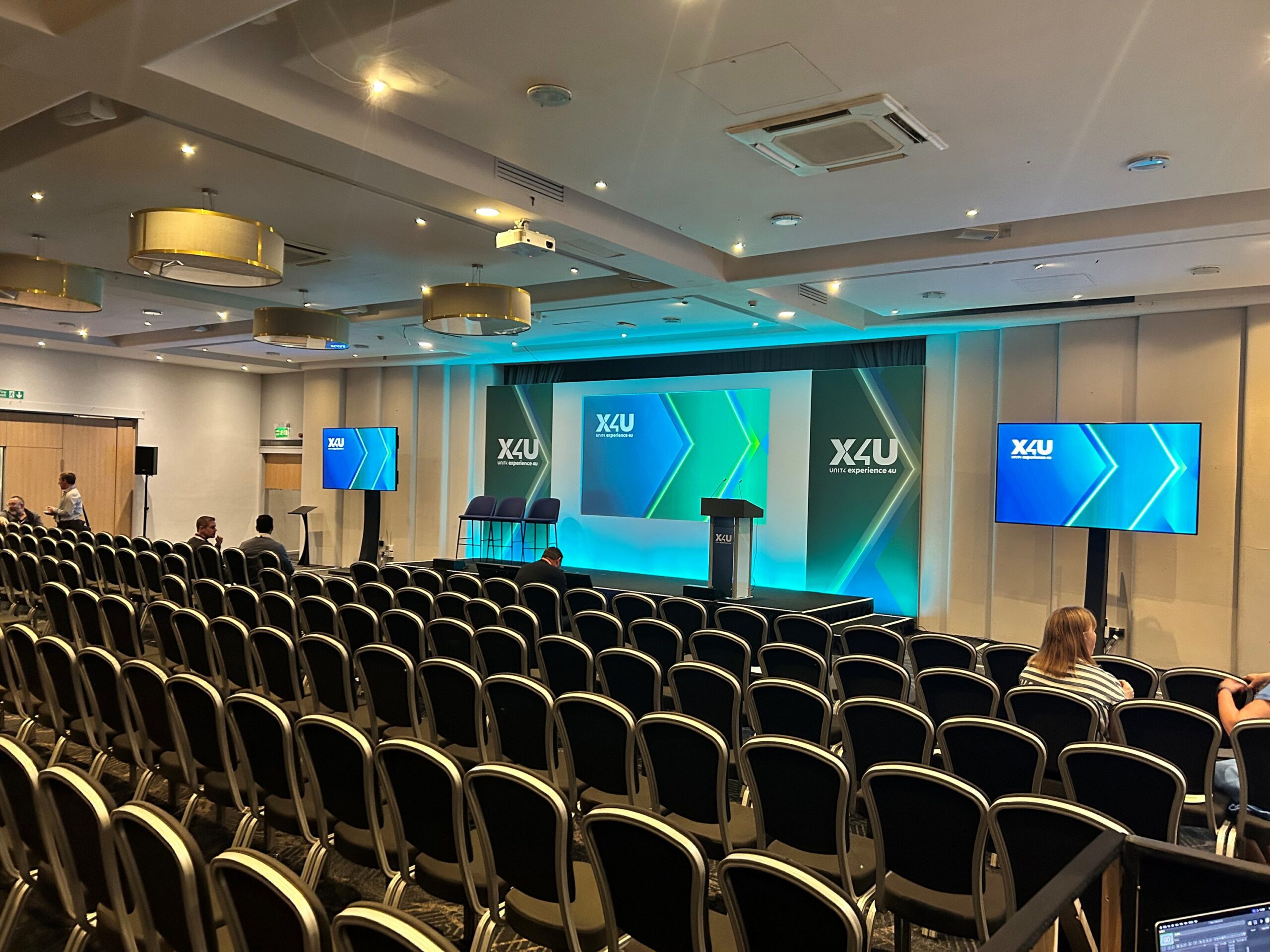 View of the stage and screen at a conference at BCEC in Birmingham, seen from behind rows of seating